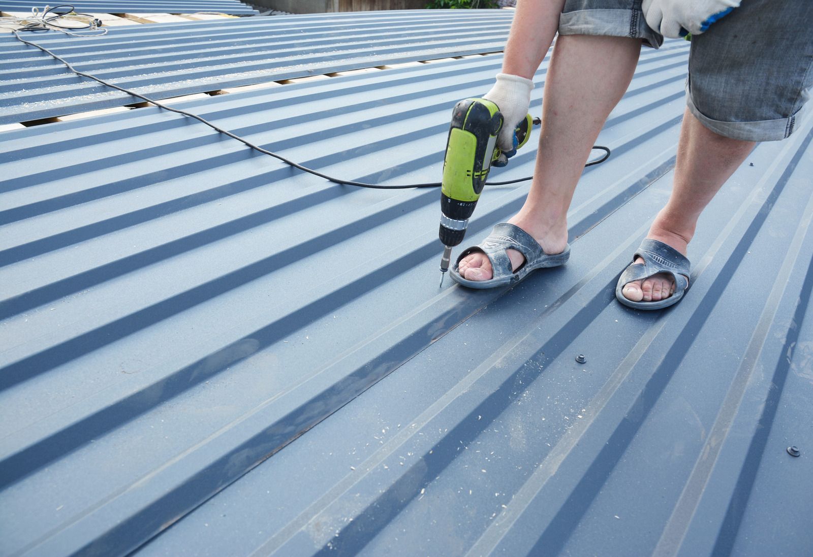 A person is using a drill on a metal roof.