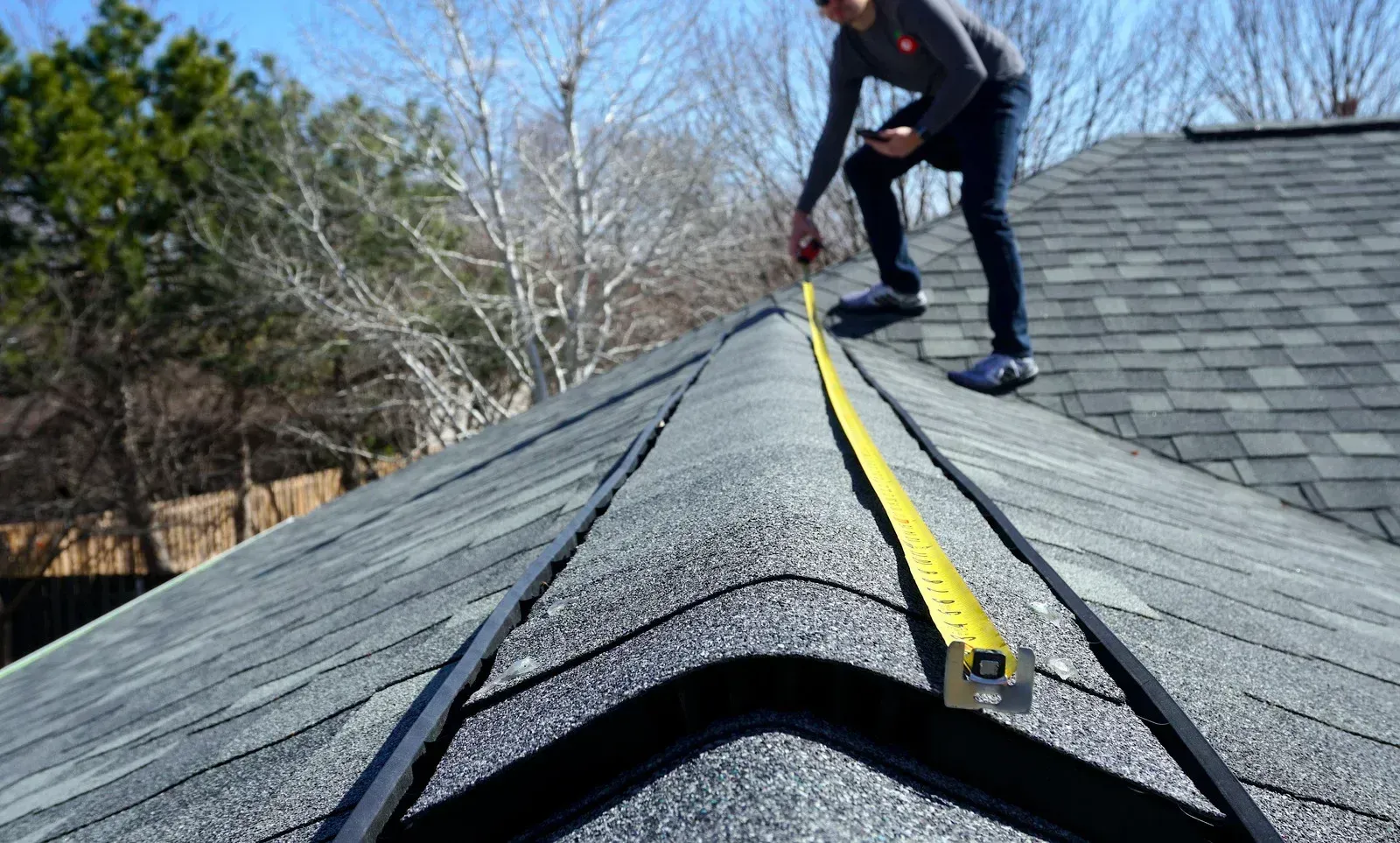 A man is measuring a roof with a tape measure.