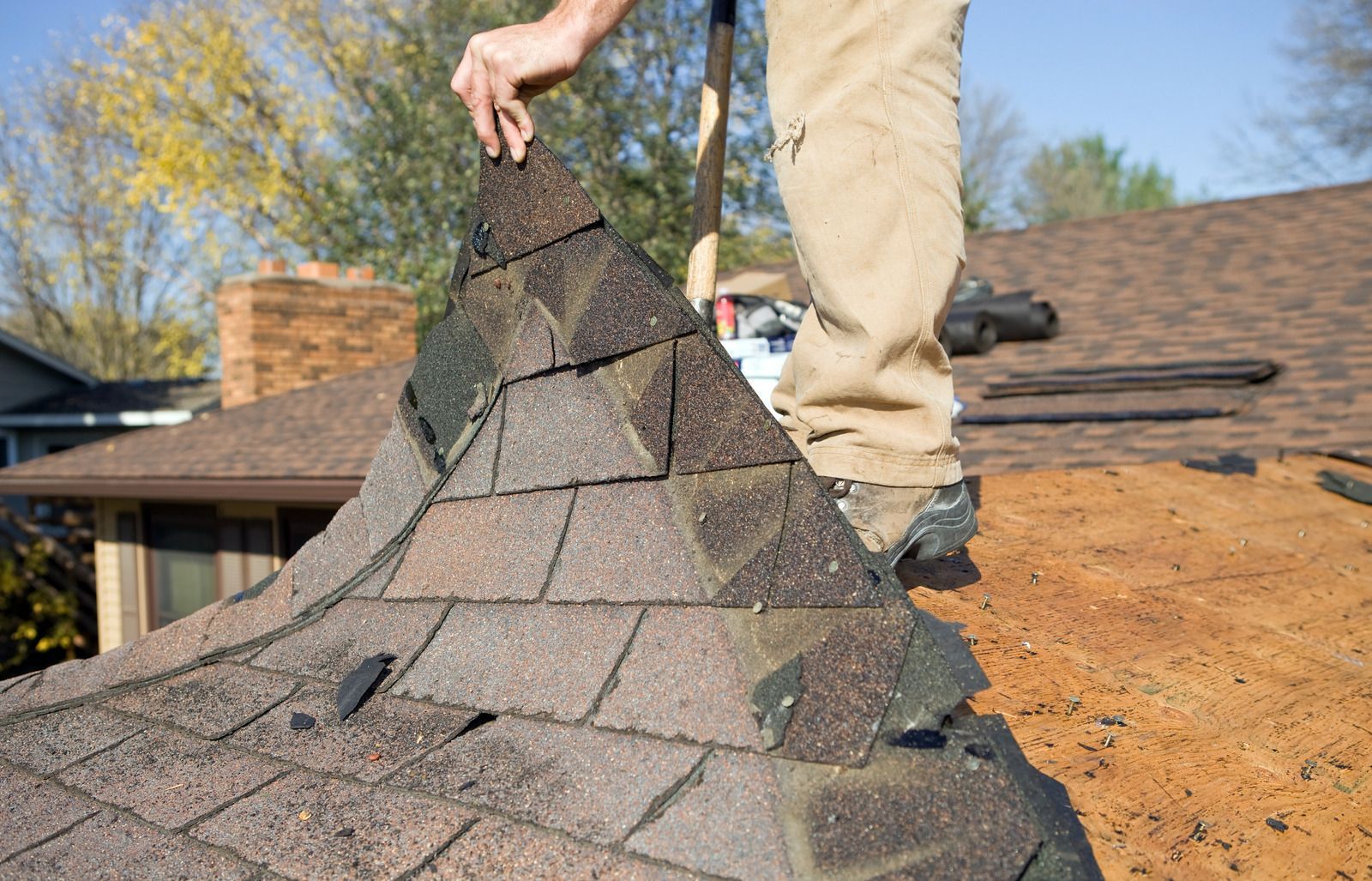 A man is standing on top of a roof holding a piece of shingles.